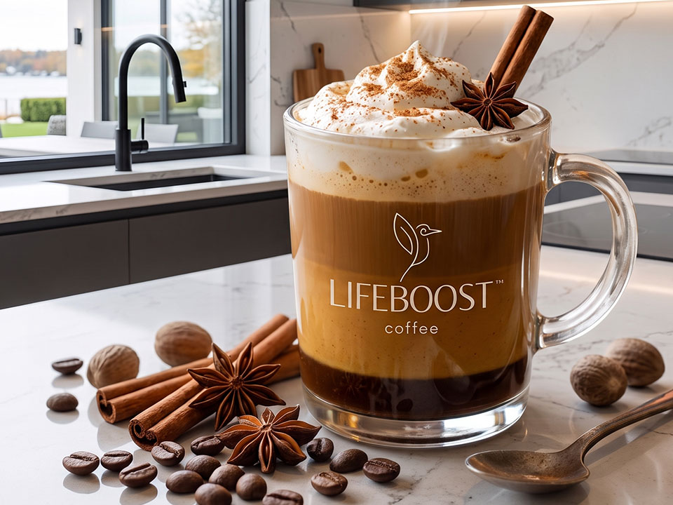A Lifeboost glass mug of pumpkin spice coffee topped with whipped cream, surrounded by cinnamon sticks, star anise, nutmeg and coffee beans