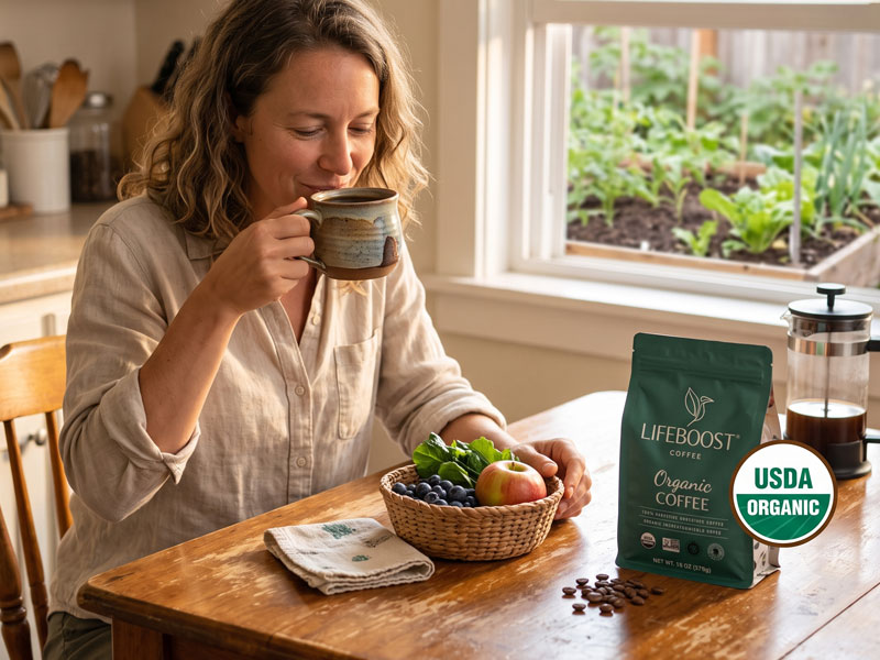 A woman drinking USDA-certified organic Lifeboost coffee at her kitchen table with fresh produce